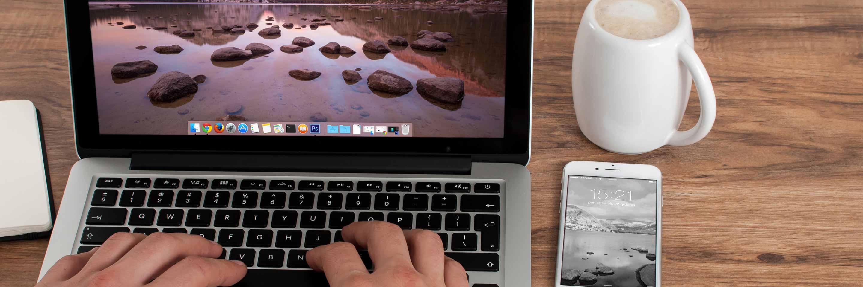 Hände tippen einen Text auf einer Laptoptastatur. Tasse Kaffee und Smartphone.